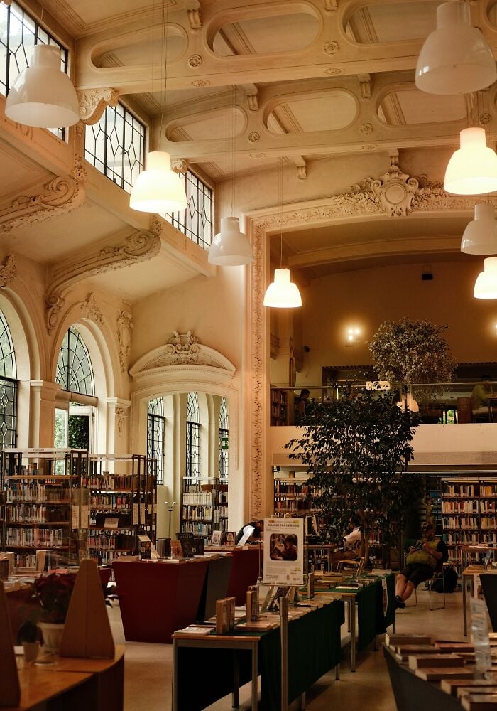 Intérieur grandiose de bibliothèque avec de hauts plafonds, une architecture ornée, de grandes fenêtres, des étagères et des coins lecture confortables.