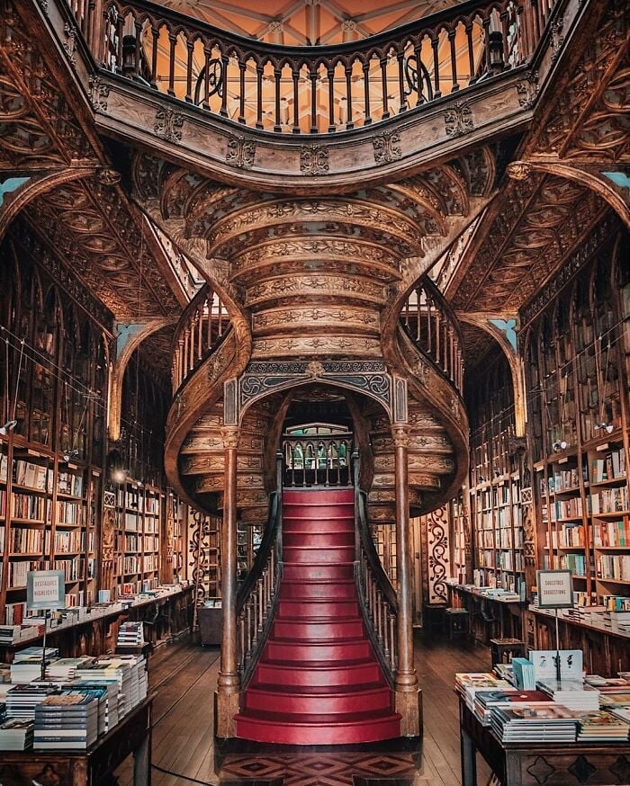 Bibliothèque grandiose et ornée avec un escalier en colimaçon en bois sculpté et des rangées de bibliothèques remplies de livres tout autour.